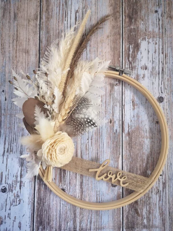 Tambour à broder orné de fleurs séchées dans les teintes crème/écrues et de plumes, comporte le mot LOVE