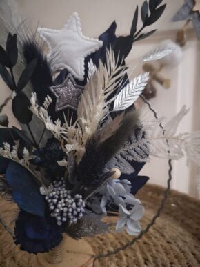 Bouquet de fleurs séchées monté sur un cercle en métal (15 cm de diamètre pour cette “petite” version) avec pied en bouleau à poser. Le bouquet est dans les tons bleus et blancs avec des touches argentées.