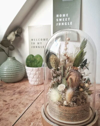 Cloche de fleurs séchées dans des tons vert, blanc et neutre.