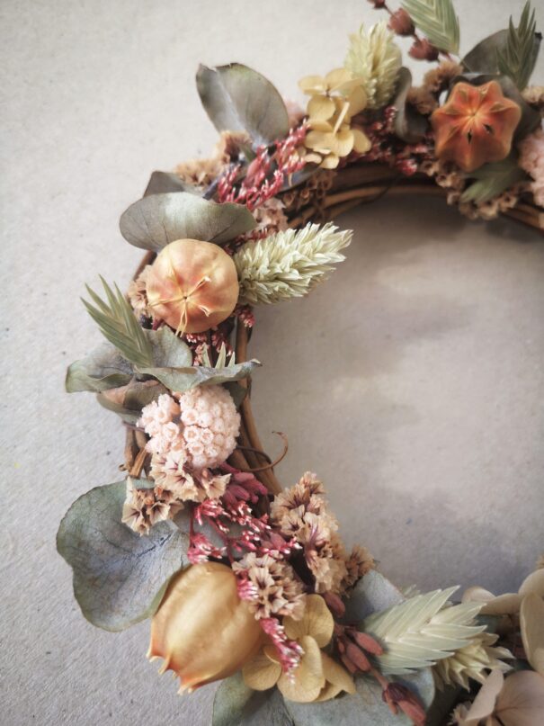 Petite couronne en sarments de vigne ornée de fleurs séchées et d’eucalyptus stabilisé dans des tons verts et roses