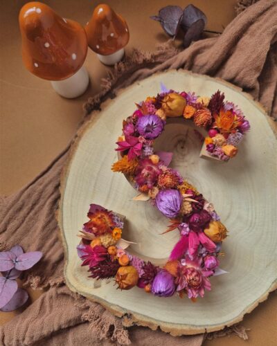 Lettre S ornée de fleurs séchées dans les tons rose, orange, violet et prune