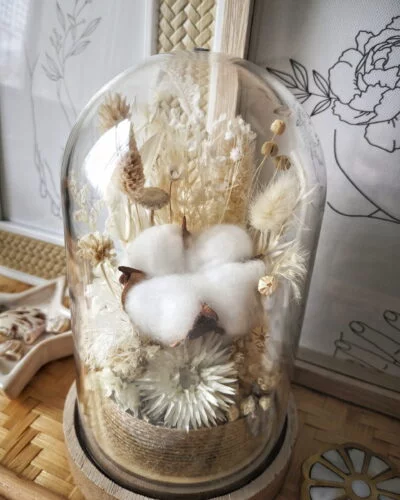 Cloche de fleurs séchées dans les tons blanc, crème et neutre. Idéale pour une décoration de mariage bohème ou pour une idée de cadeau pour un 1er anniversaire de mariage (noces de coton) grâce à sa fleur de coton située au centre de la cloche.