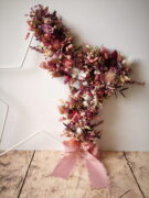 Etoile ornée de fleurs séchées dans les tons rose, doré et violet. Cette couronne en forme d’étoile pourra être suspendue ou posée.