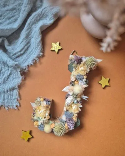 Lettre "J" ornée de fleurs séchées dans les tons blanc, bleu, vert