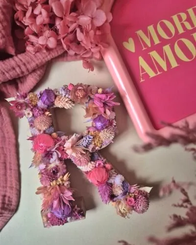 Lettre “R” ornée de fleurs séchées dans les tons rose, violet et pêche